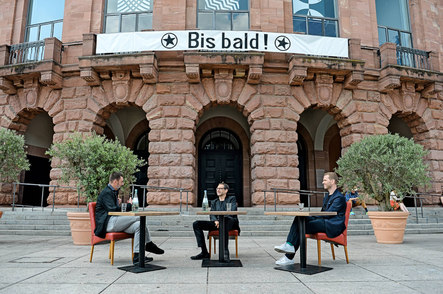 DdB-Chefredakteur Detlef Brandenburg, Intendant Markus Müller und Bühnenbildner Sebastian Hannak vor der Fassade des Staatstheaters Mainz.