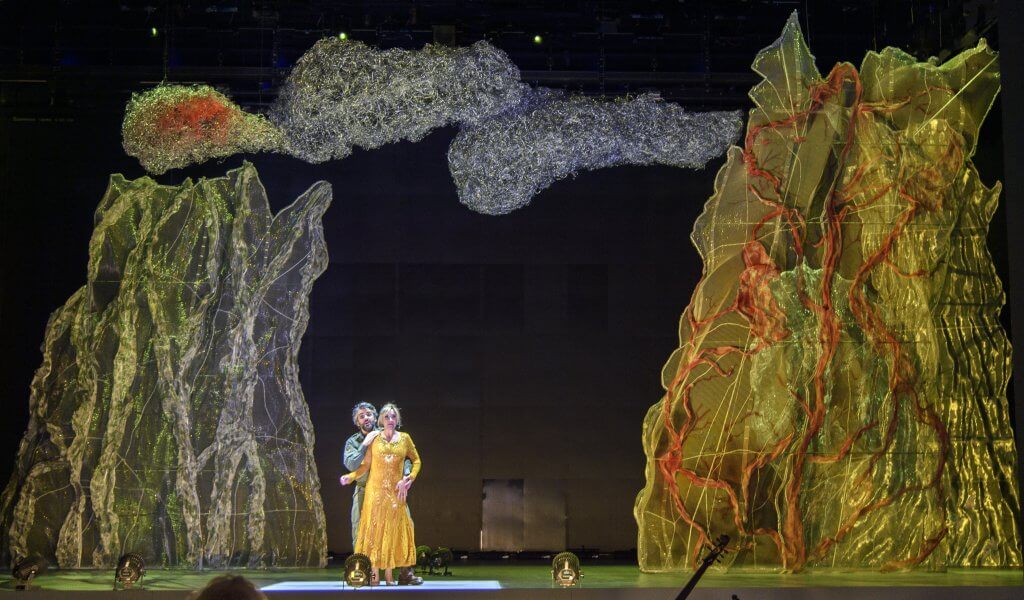 Auf einer Bühne mit zwei künstlerisch verfremdeten Bäumen umarmen sich zwei Menschen.