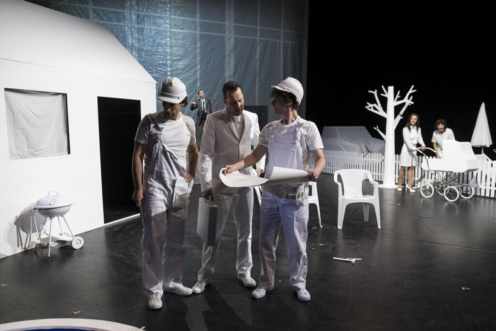 Drei Personen in Weiß stehen zwischen weißer Pappdeko und schienen über Pläne auf Papier zu diskutieren.