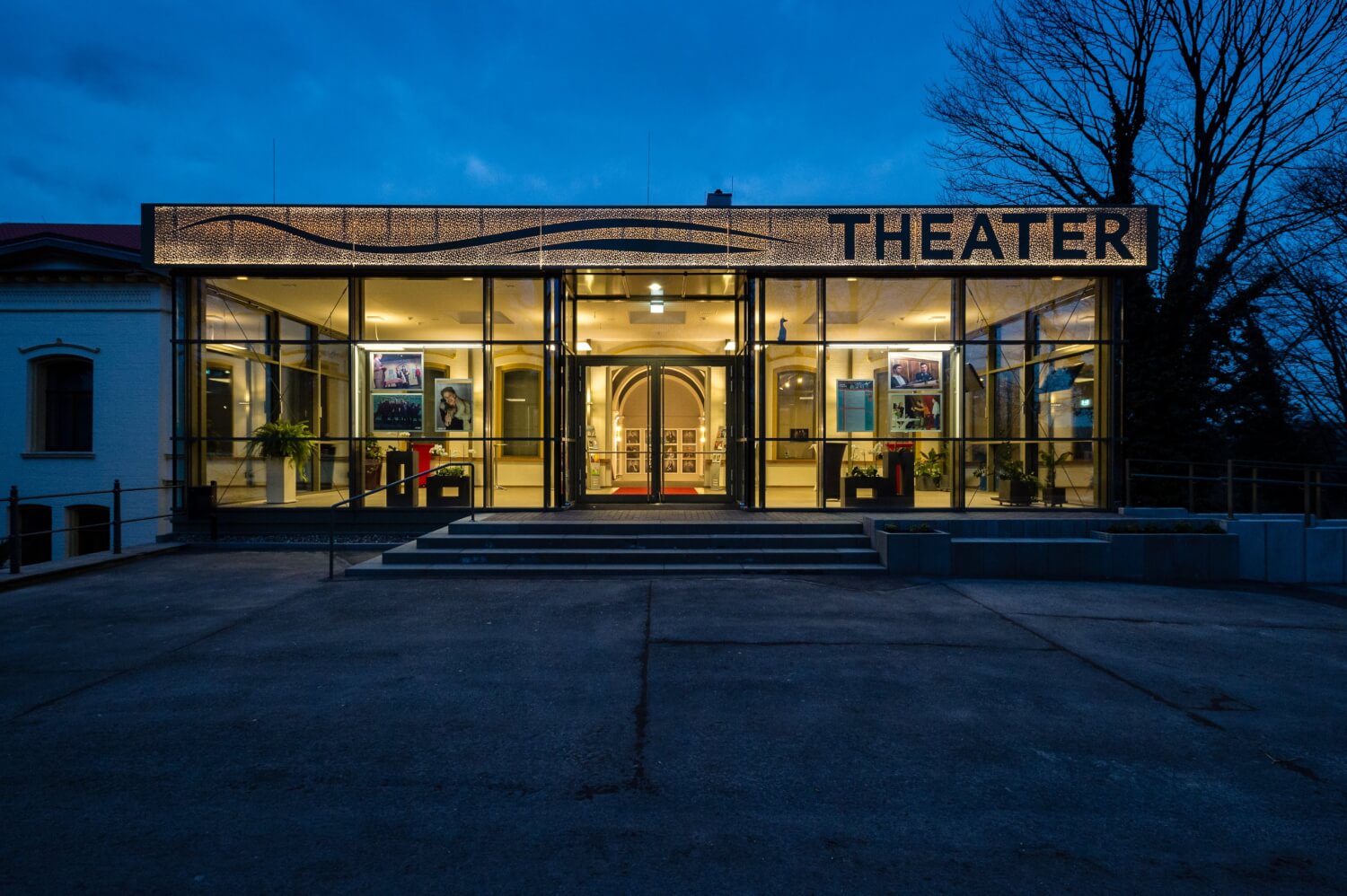 Blick auf das verglaste und erleuchtete Foyer bei Dämmerung.