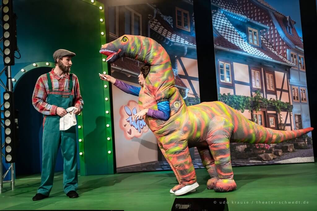 Eine Person in einem Dinosaurier-Kostüm bietet einem Mann einen Joint an.