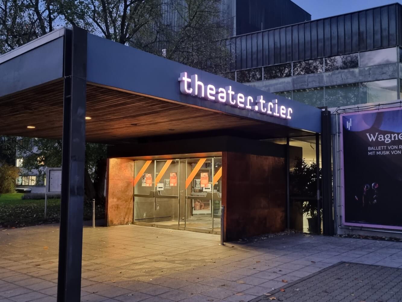 Theater Trier Haupteingang Zu sehen ist der Haupteingang des Theater Trier in der Dämmerung. Die Eingangstüren sind beleuchtet.