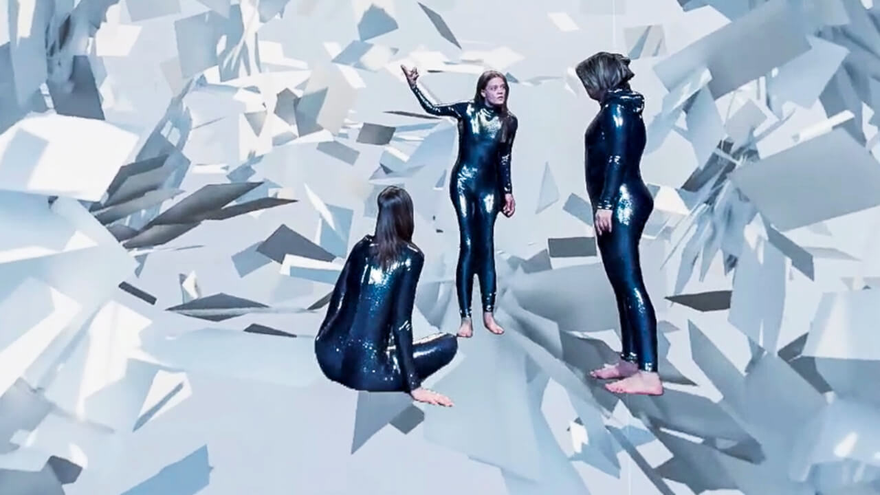 Marie Schulte-Werning, Lea Reihl und Gabriella Weber stehen inmitten einer zerfallenden Landschaft. Um sie herum ragen spitze Stücke in den Raum hinein und umzingeln sie.