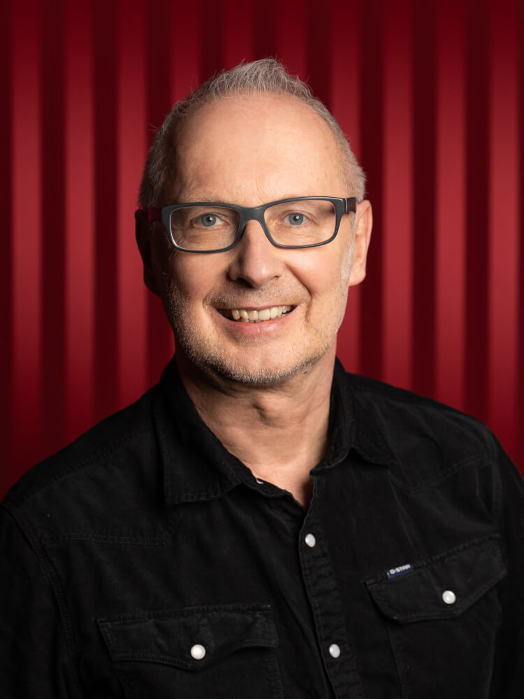 Zu sehen ist Frank Behnke, Schauspieldirektor am Staatstheater Meiningen, vor einem roten Vorhang
