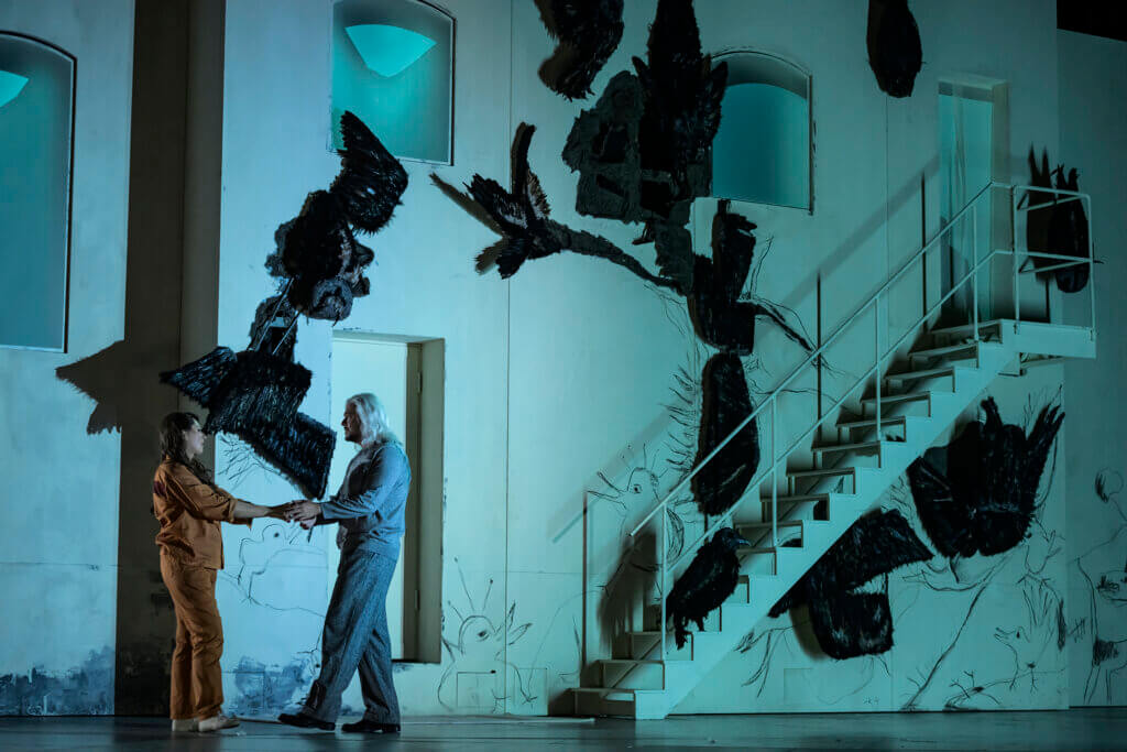 Elsa und Lohengrin stehen vor einer weißen Wand mit Raben.