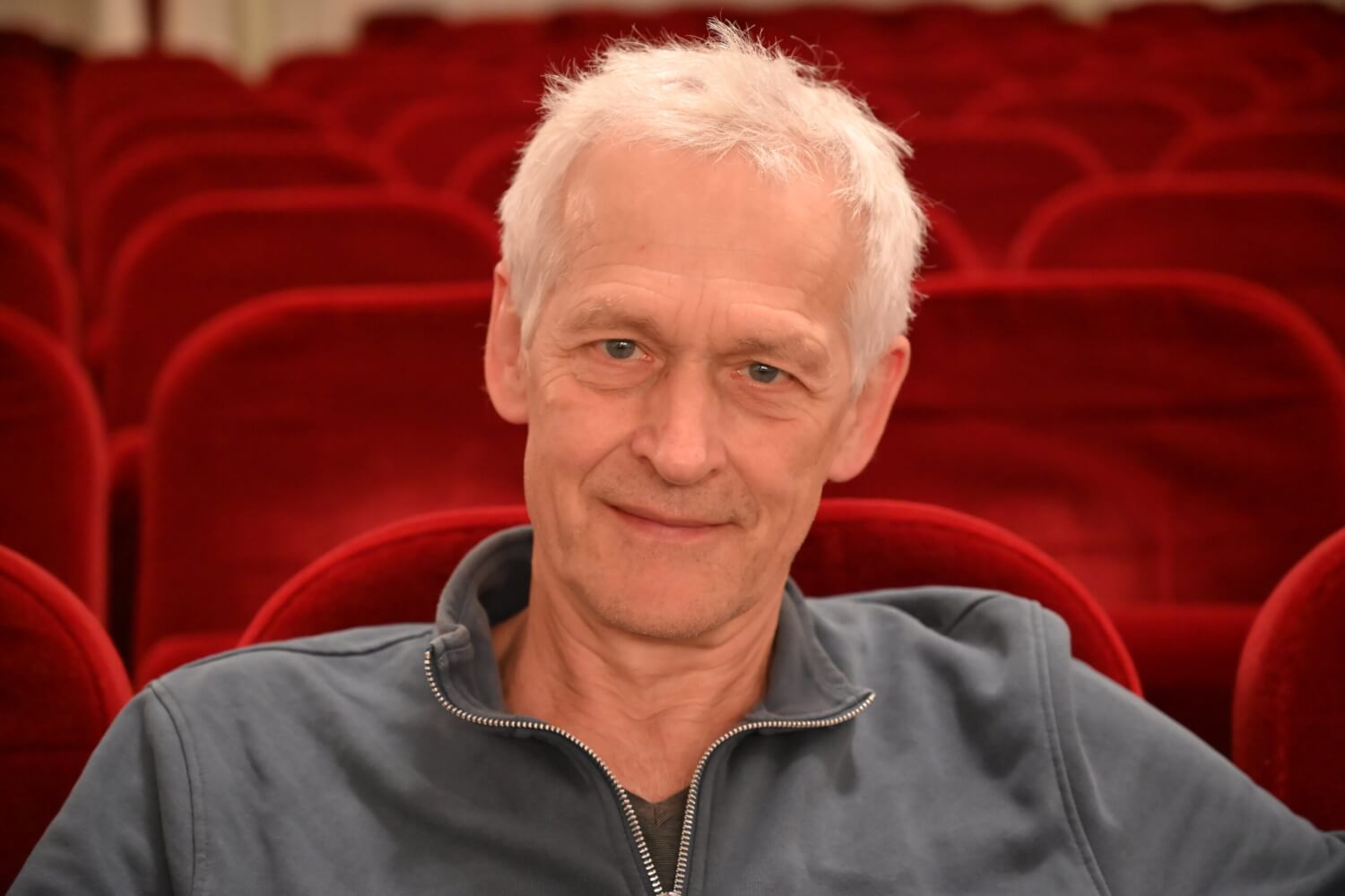 Zu sehen ist eine Nahaufnahme von Andris Plucis, kommissarischer Schauspielleiter am Landestheater Eisenach. Er sitzt im Zuschauerraum, die Sitze sind mit rotem Samt bezogen.