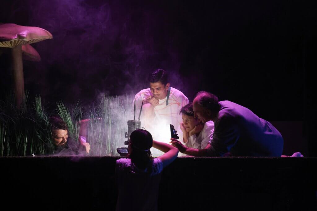 Szenenfoto aus „Der Zauberer von Öz – Eine Fußballtragödie“ von Akın Emanuel Şipal am Theater Bremen. Fünf Schauspieler:innen knien, liegen oder stehen um etwas hell Erleuchtetes in der Mitte und schauen darauf.