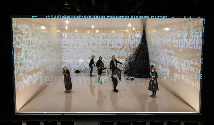 Mehrere Personen stehen in einem weißen Raum mit Textprojektionen.