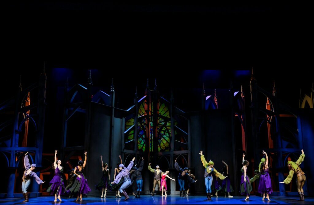 Die Tänzer:innen verteilt vor einem großen runden Kirchenfenster.