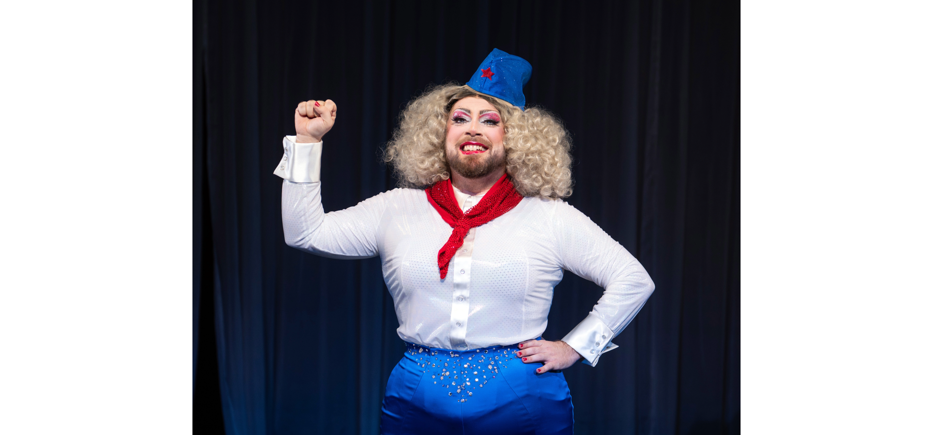 eine Person im traditionell inspirierten Dragkostüm mit erhobener rechter Faust