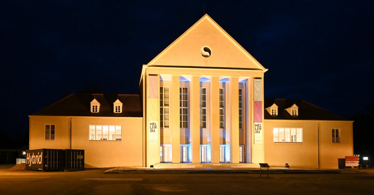 Festspielhaus Hellerau bei Nacht. Die helle Fassade ist in warmem Licht erleuchtet.