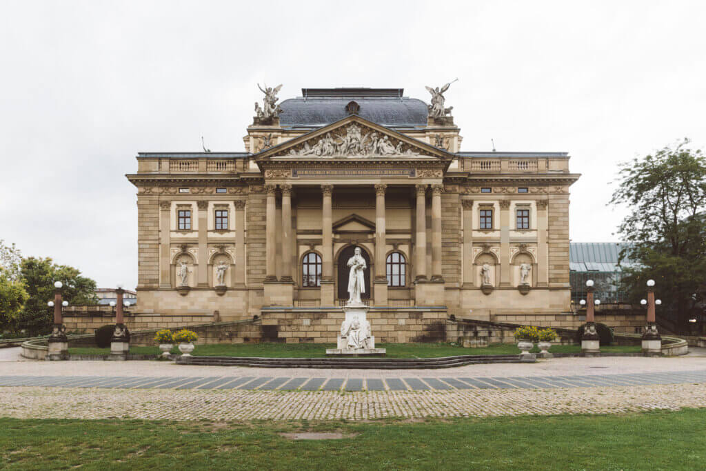 Das Gebäude des Staatstheater Wiesbaden seitlich fotografiert aus Richtung des Kurparks. Vor dem Gebäude eine Statue.