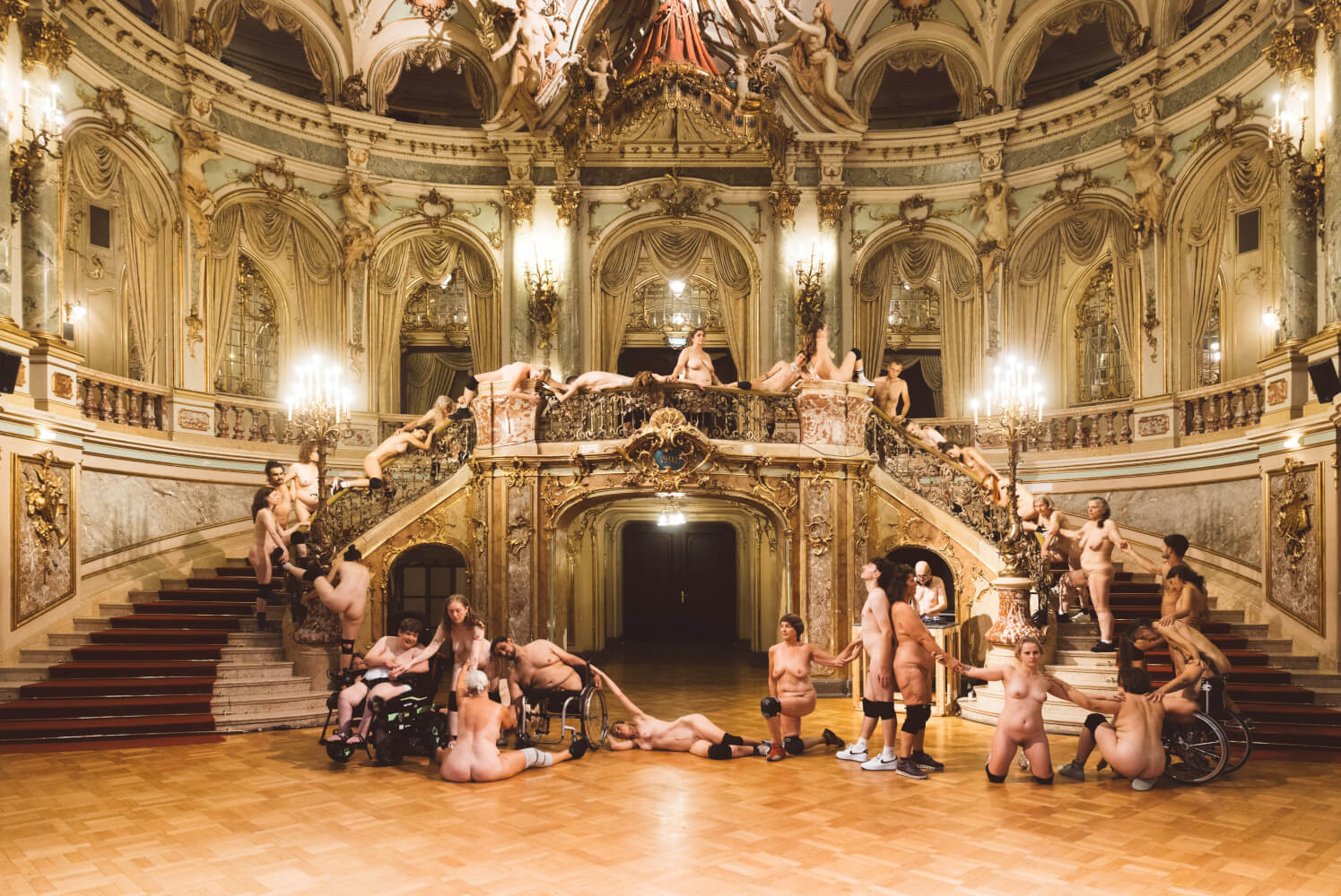 Tanzspektakel „Habitat” von Doris Uhlich am Staatstheater Wiesbaden. Im prunkvollen Foyer säumen den Treppenaufgang nackte Körper, manche Menschen sitzen im Rollstuhl und tragen schwarze Knieschoner, sie halten sich an den Händen.