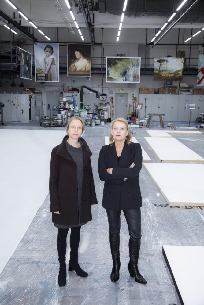Dorothea Hartmann (l.) und Beate Heine (r.) im Malsaal des Staatstheater Wiesbaden. Weiße Flächen auf dem Boden und an der Decke hängende Gemälde im Hintergrund.