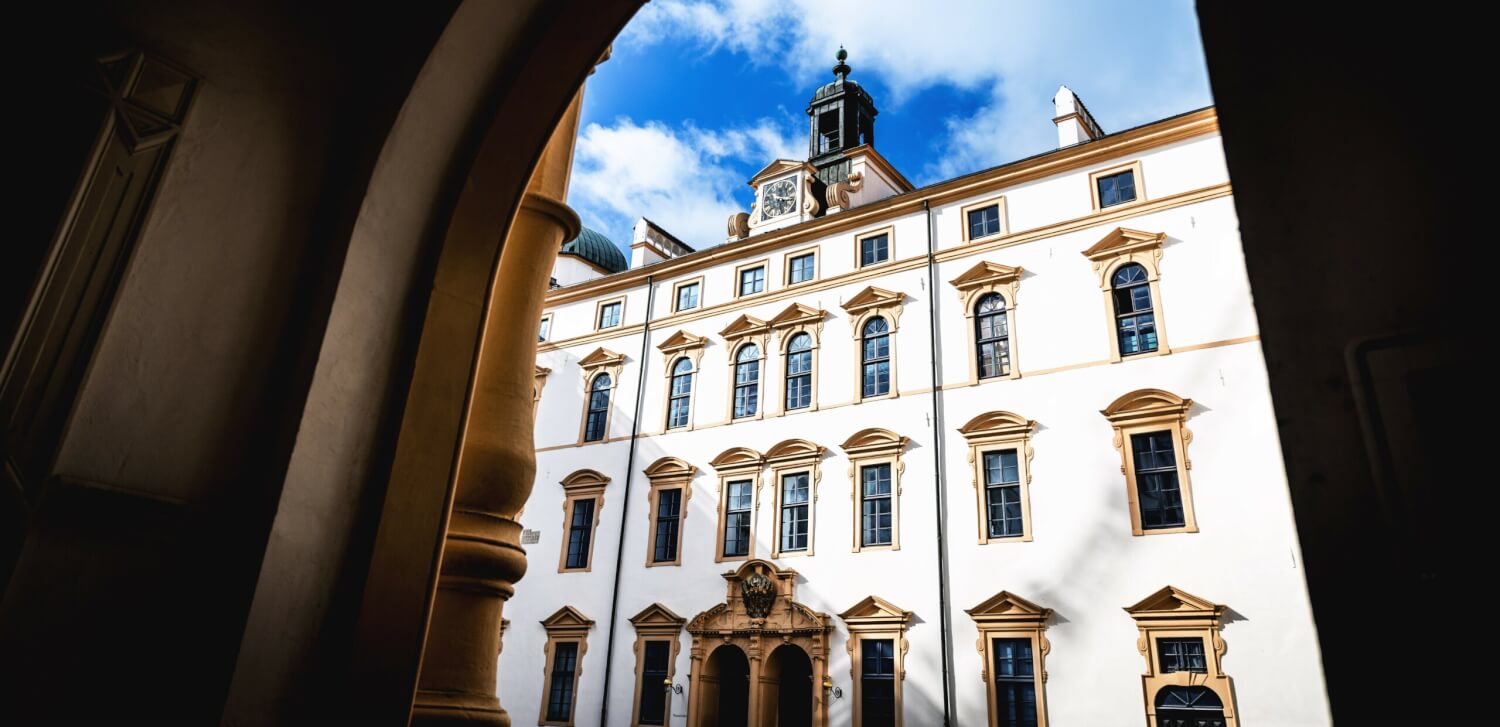 Das Schlosstheater Celle durch einen Torbogen fotografiert. Das Gebäude liegt in der Sonne, am Himmel sind weiße Wolken.