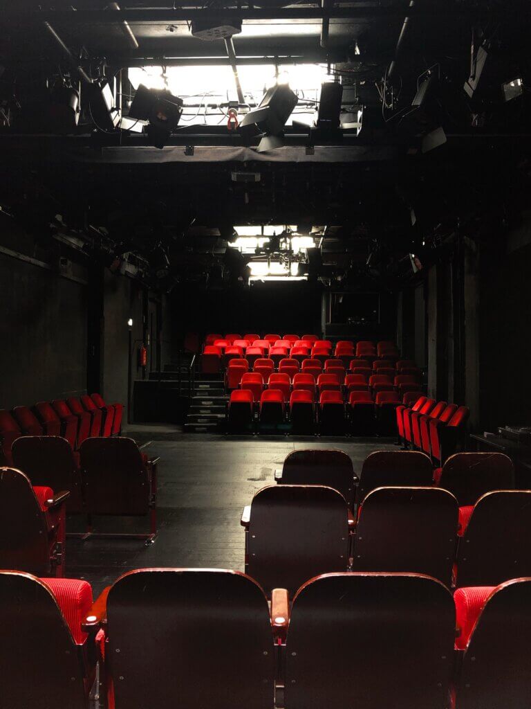 Theater in der Garage am schauspiel erlangen. Schwarzer Bühnenboden in der Mitte, umrandet von samt-roten Zuschauersitzen.