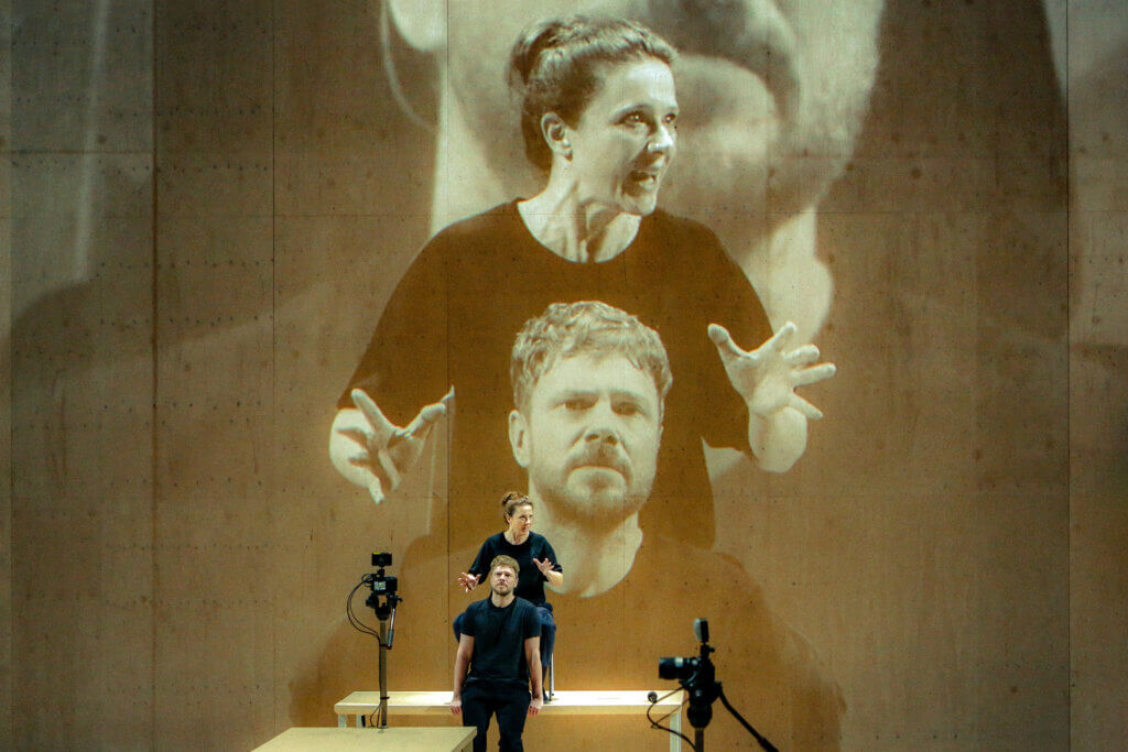 zwei Personen auf einer Bühne, dahinter noch einmal größer projiziert