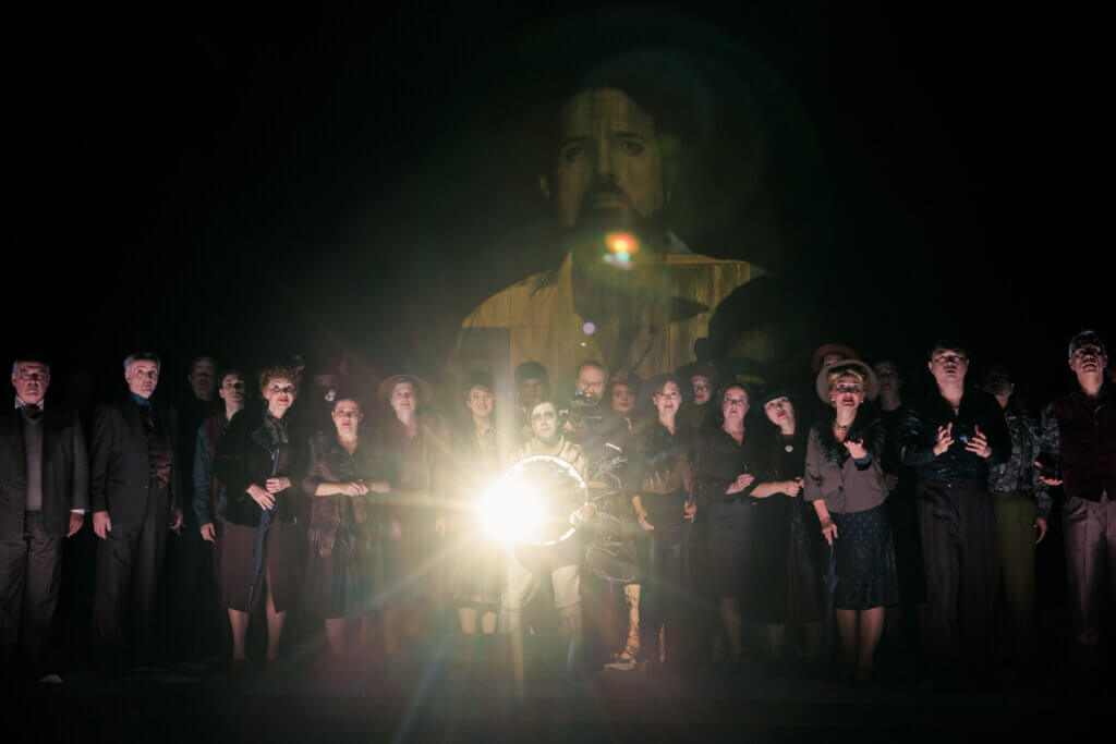 Ein Ensemble auf der dunklen Bühne, ein helles Licht strahlt aus ihrer Mitte