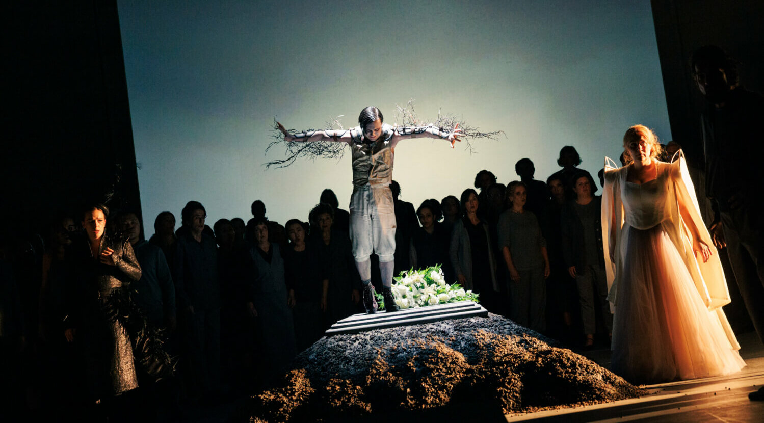 Eine Person mit ausgestreckten Armen mit befestigten zweigen auf einem Grab, dahinter der Chor