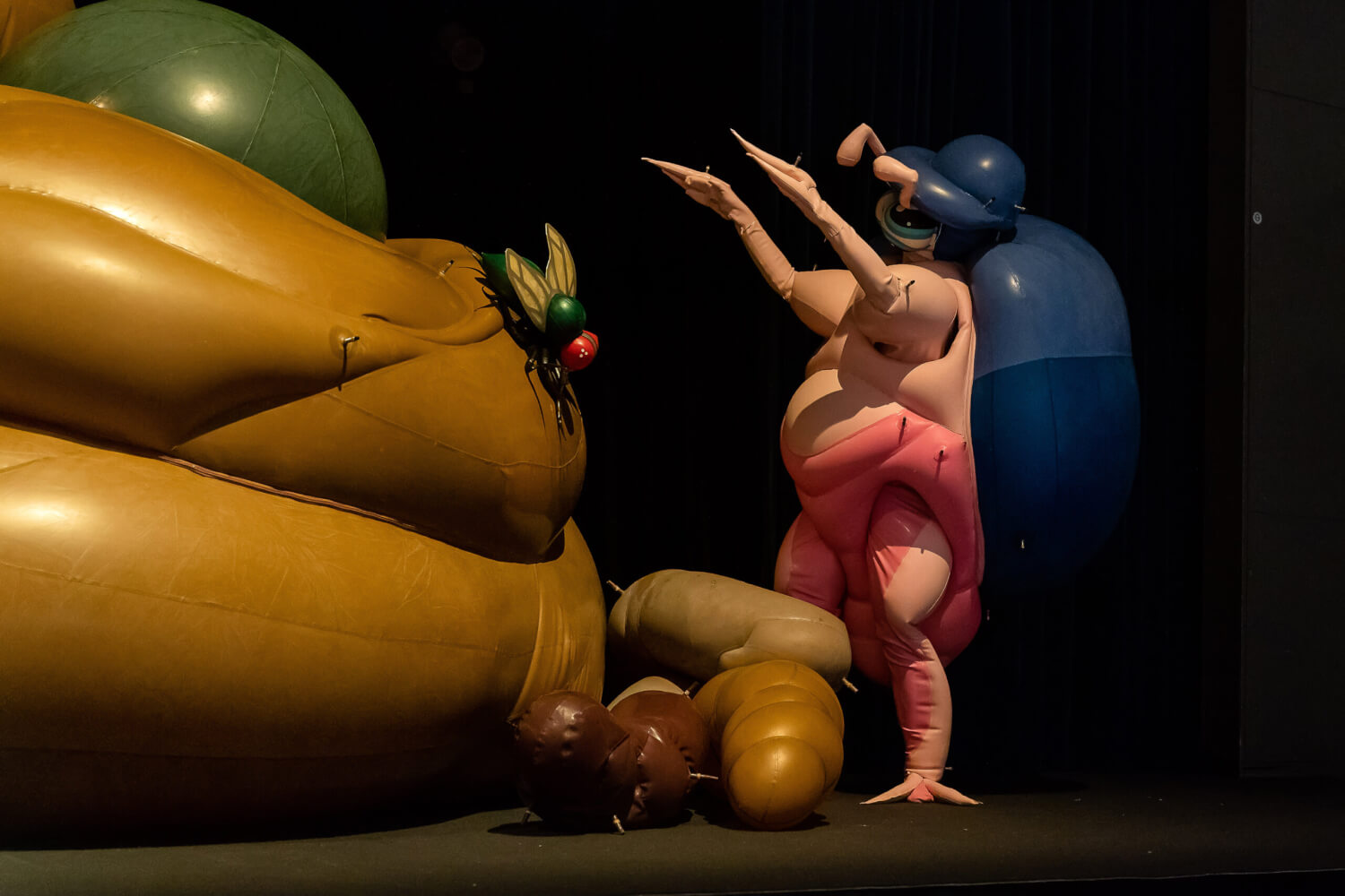 Aufführungsfoto von „Super Farm“ der Künstlerin Saeborg. Mehrere aufblasbare Gummitiere und Objekte. Links sitzt eine Schmeißfliege auf einem Kackhaufen.