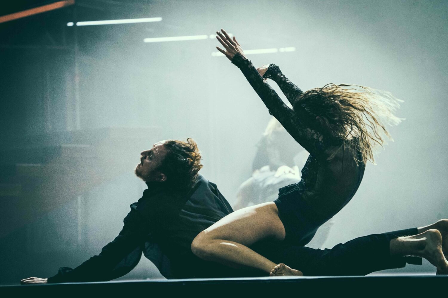 James Potter und Terra Hunter Kell in der Uraufführung von „Der Tod und das Mädchen“ am Staatstheater Kassel. Eine Frau sitzt auf dem Rücken eines Mannes, der mit dem Bauch auf dem Boden liegt. Sie reißt die Arme nach oben.