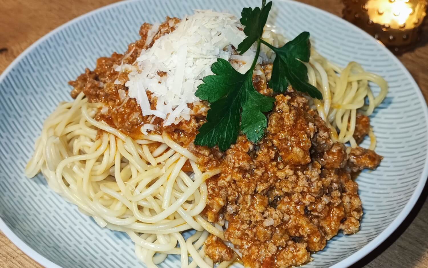 Ein Teller mit Spaghetti Bolognese. Auf dem Hackfleisch liegen Parmesanspähne und Petersilie.