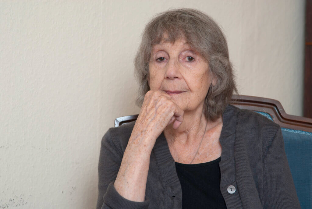 Porträt von Gerlind Reinshagen. Sie sitzt auf einem Stuhl, die rechte Hand am Kinn angelehnt.