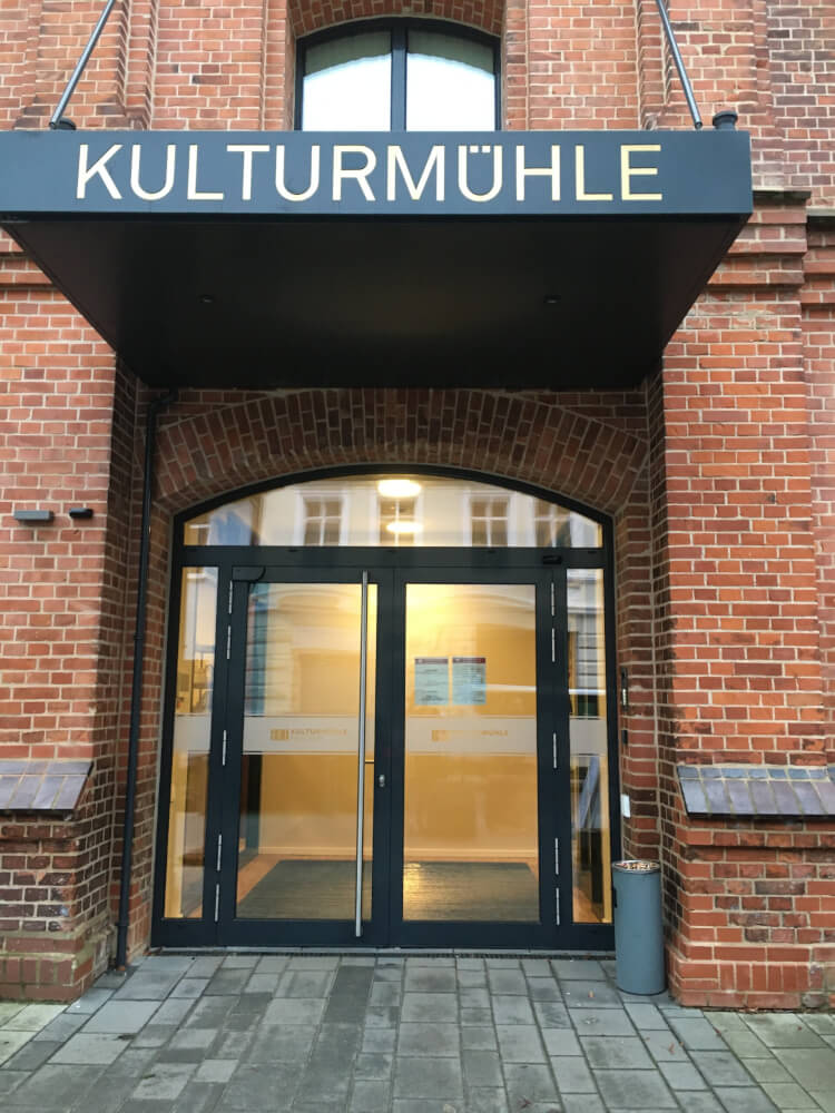 Der Eingang der Kulturmühle des Jungen Staatstheater Parchim. Rotes Backsteingebäude, über dessen Eingang in großen Lettern Kulturmühle steht.
