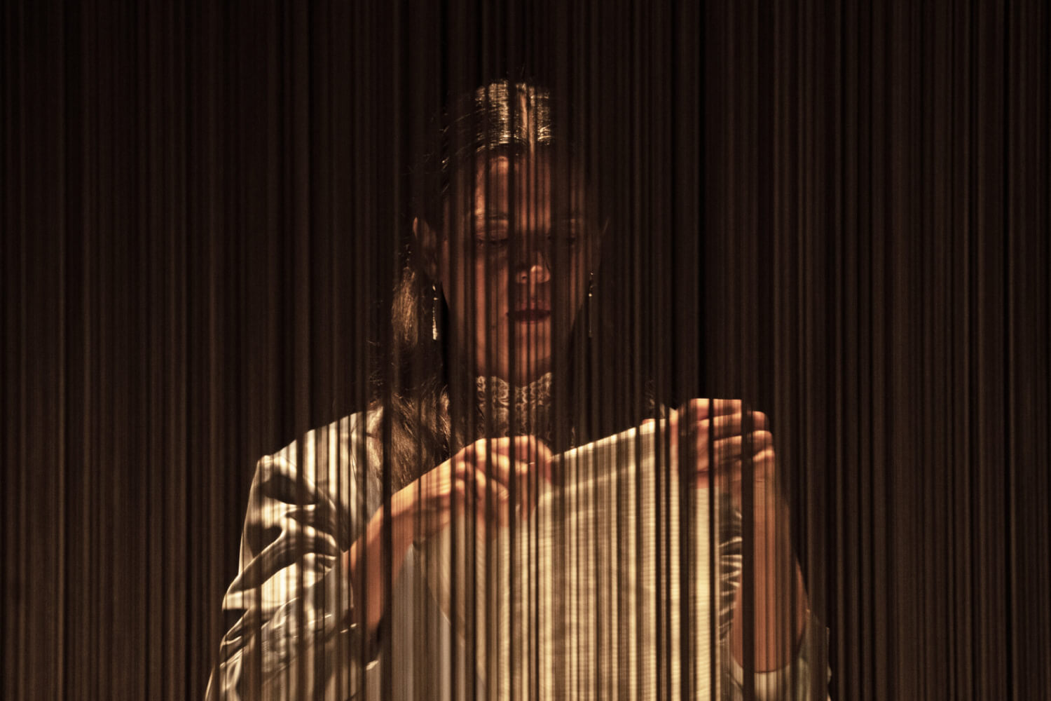 Aufführungsfoto von „Söhne“ von Marine Bachelot Nguyen am Schlosstheater Moers. Eine Frau steht hinter einem Fadenvorhang und hält ein Tuch in ihren Händen.