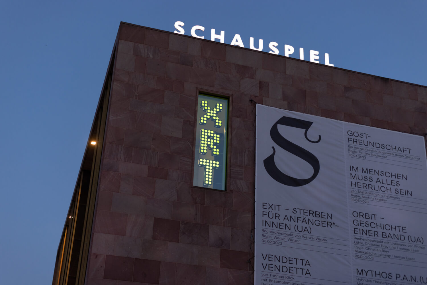 Die Fassade des Staatstheaters Nürnberg mit der neuen digitalen Spielstätte XRT in der Dämmerung. Die Letter des Schauspiel und XRT sind hell erleuchtet.