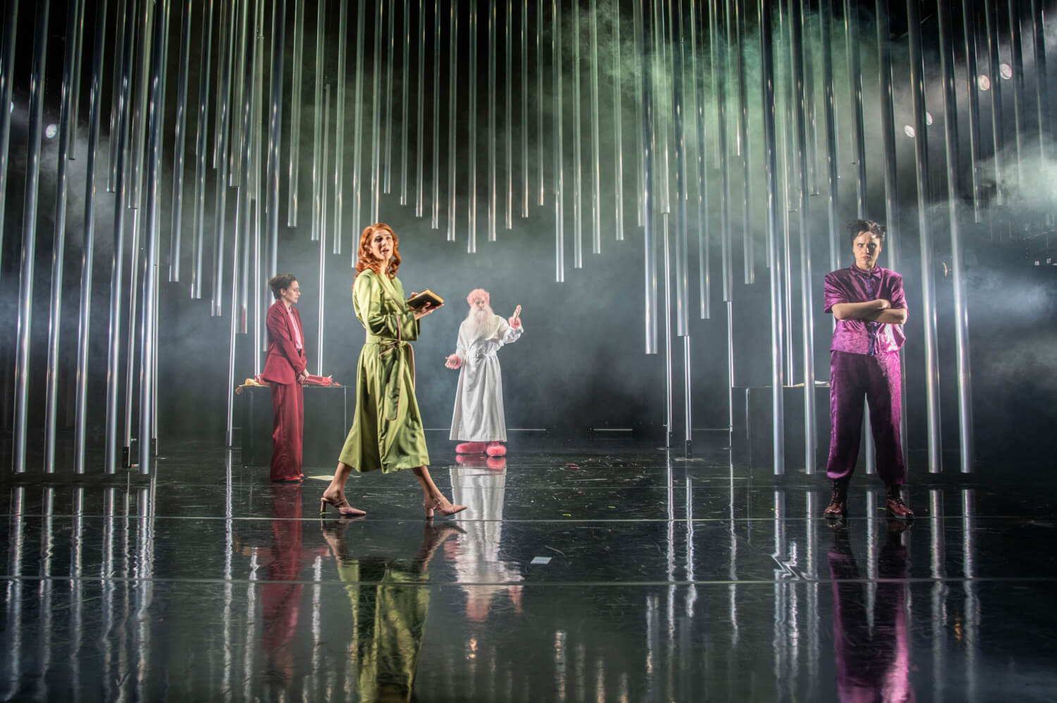 „Die Hölle auf Erden“ von Maria Lazar am Theater Magdeburg. Auf dunkel spiegelndem Boden stehen vier Personen. Von oben ragen silberne Röhren, die wie Orgelpfeifen aussehen nach unten.