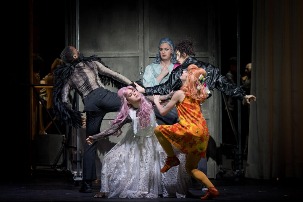 Eine darstellende Person im babyblauen Kleid wird von vier Tänzer:innen umringt