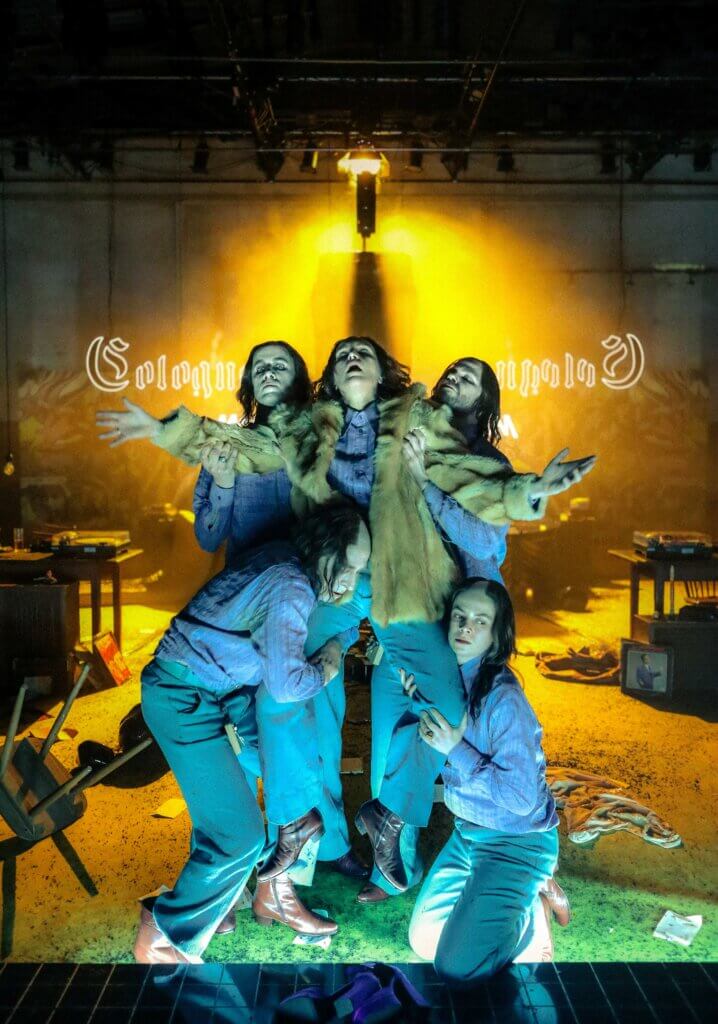 Fünf Darsteller:innen. Eine in der Mitte von den anderen gehalten, dahinter gelbes Licht