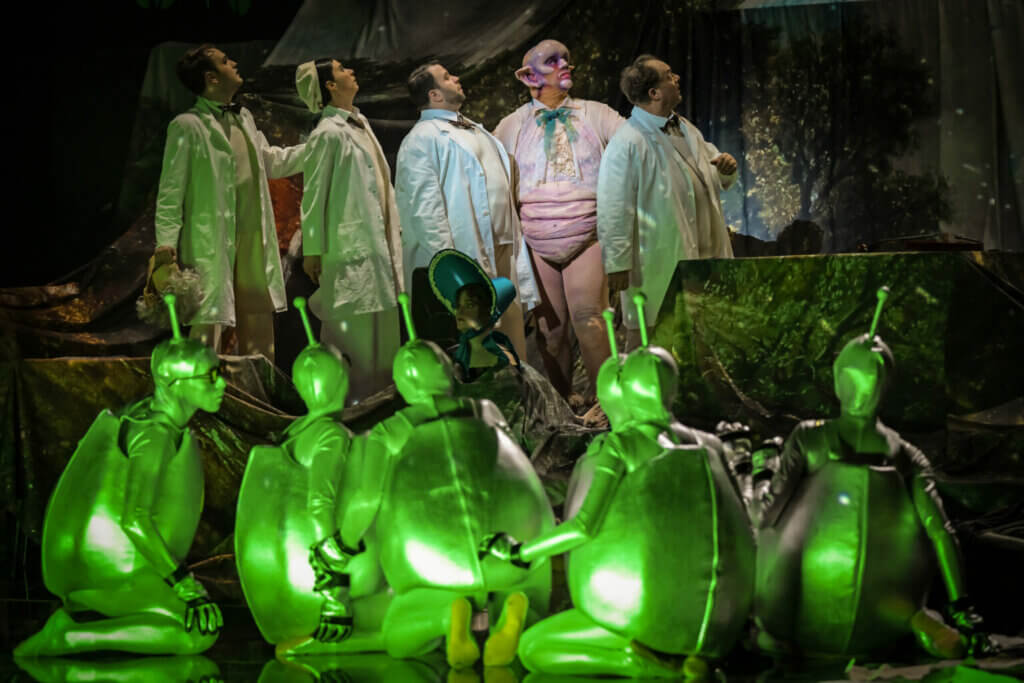 im Vordergrund grün verkleidete Aliens, dahinter das Ensemble