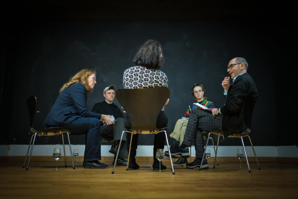 Fünf Personen sitzen im Kreis und unterhalten sich.
