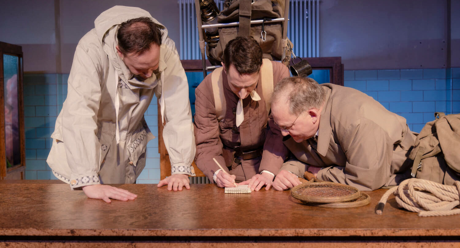 Wiard Witholt, Florian Mania, Gerald Fiedler beugen sich alle über einen Tisch und schauen Florian Mania zu, wie er auf einem Zettel schreibt.