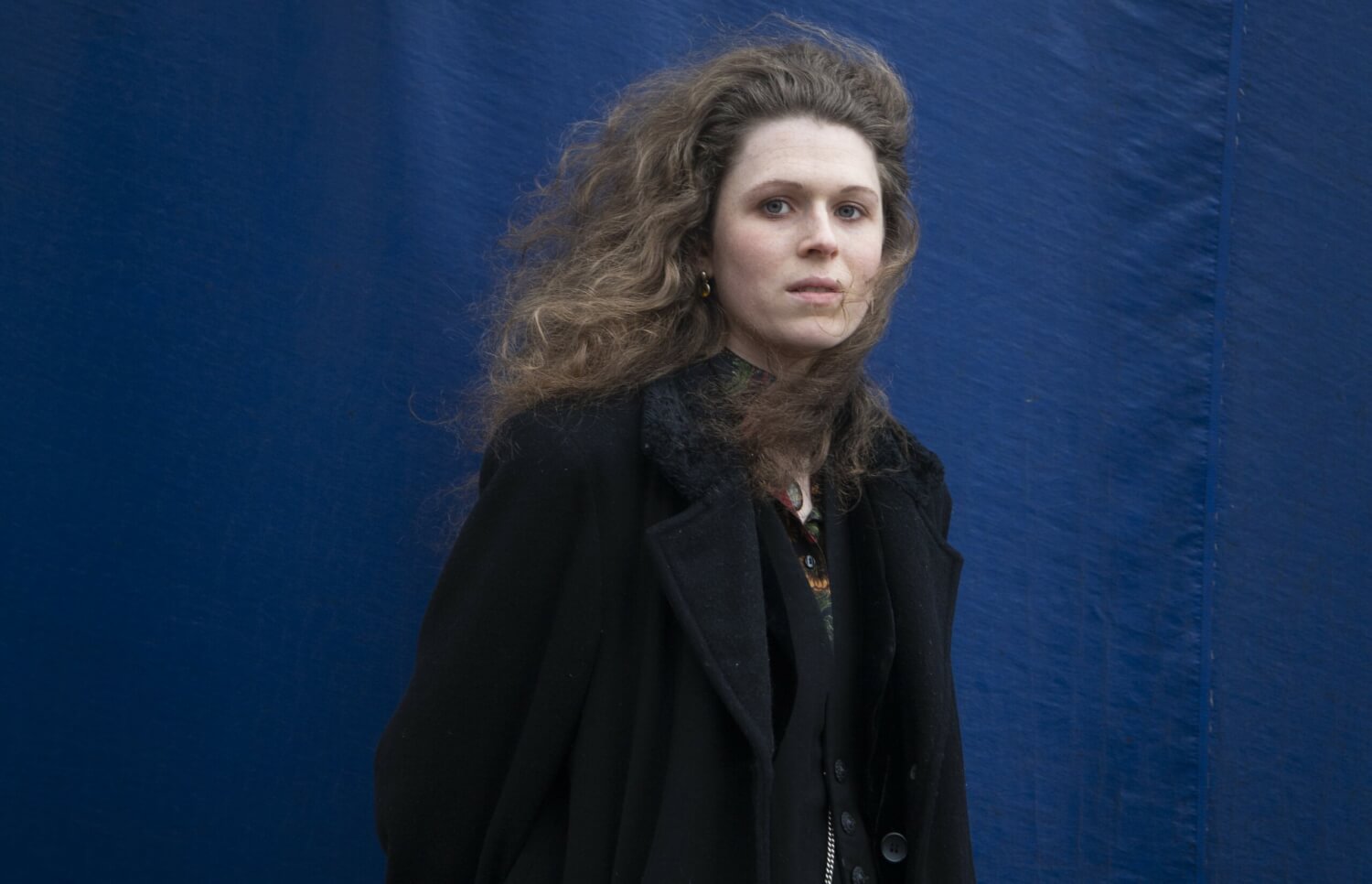 Ein Porträt von Cosmea Spelleken vor einer blauen Stoffwand.