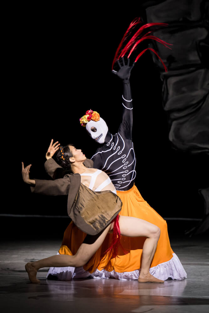 Aufführungsfoto von „Frida“ von Annabelle Lopez Ochoa am Theater Dortmund mit Sae Tamura und Simon Jones. Der Tänzer trägt ein Sensenmann-Kostüm und hält die Tänzerin im Arm, die ihn anblickt.