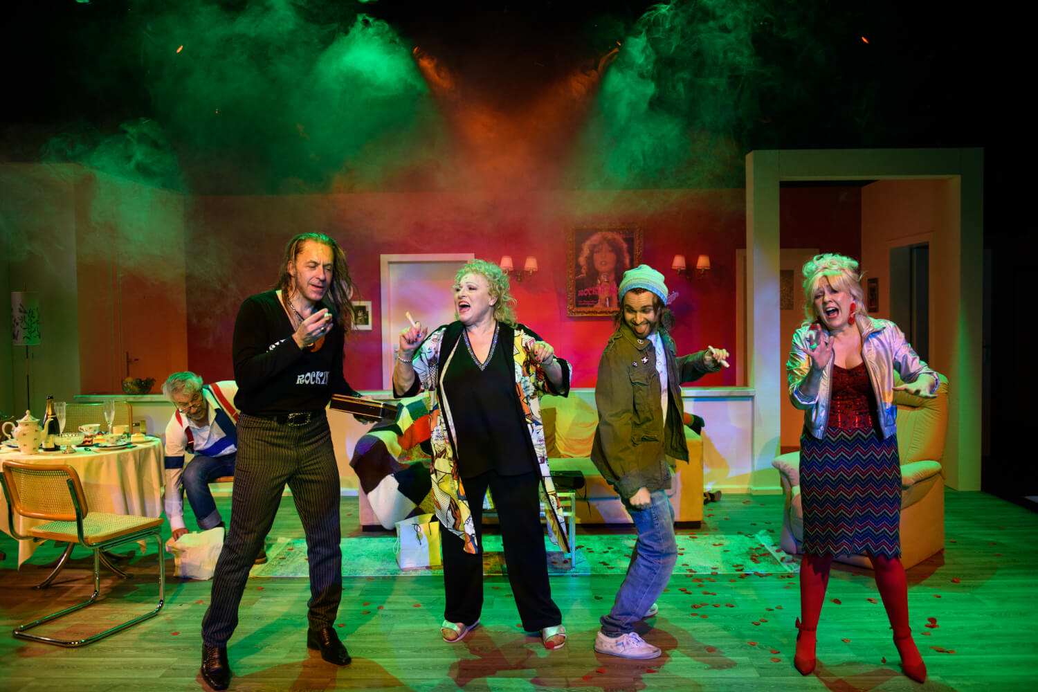 Szene aus „Rockin’ Rosie“ am Münchner Gärtnerplatztheater. Zwei Männer und zwei Frauen stehen singend und tanzend nebeneinander im grünen Scheinwerferlicht in einer Zimmerkulisse.
