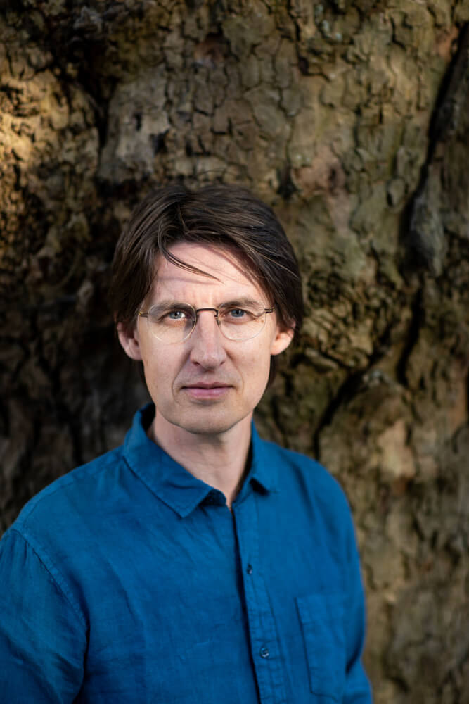 Simon van den Berg steht vor einem Baum.