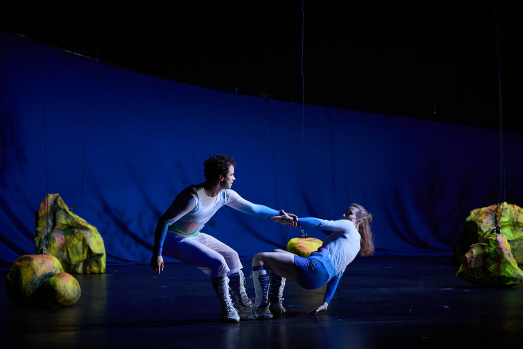 Alban Mondschein und Marie Dziomber halten sich an der Hand, ziehen sich vom Boden hoch. Die Bühne ist in beklemmendes Licht getaucht.