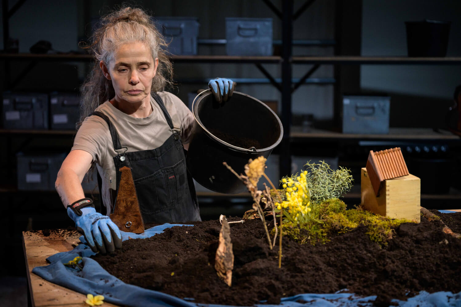 Daniela Mohr steht links im Bild. Sie trägt eine Schürze und Handschuhe und verteilt Erde auf einem Tisch.