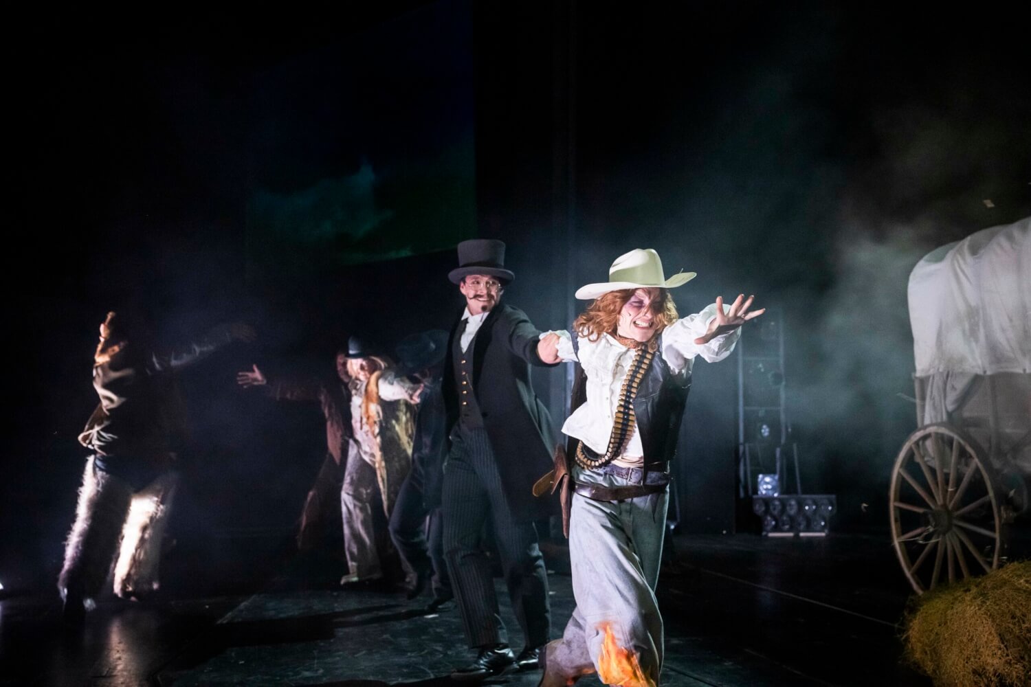 Auf der Bühne ist es nebelig und dunkel. Peter Rahmani, Sebastian Kremkow, Anne Eigner sind in einen Konflikt verwickelt. Kremkow versucht Eigner am Arm zurückzuziehen und vom Fliehen abzuhalten.