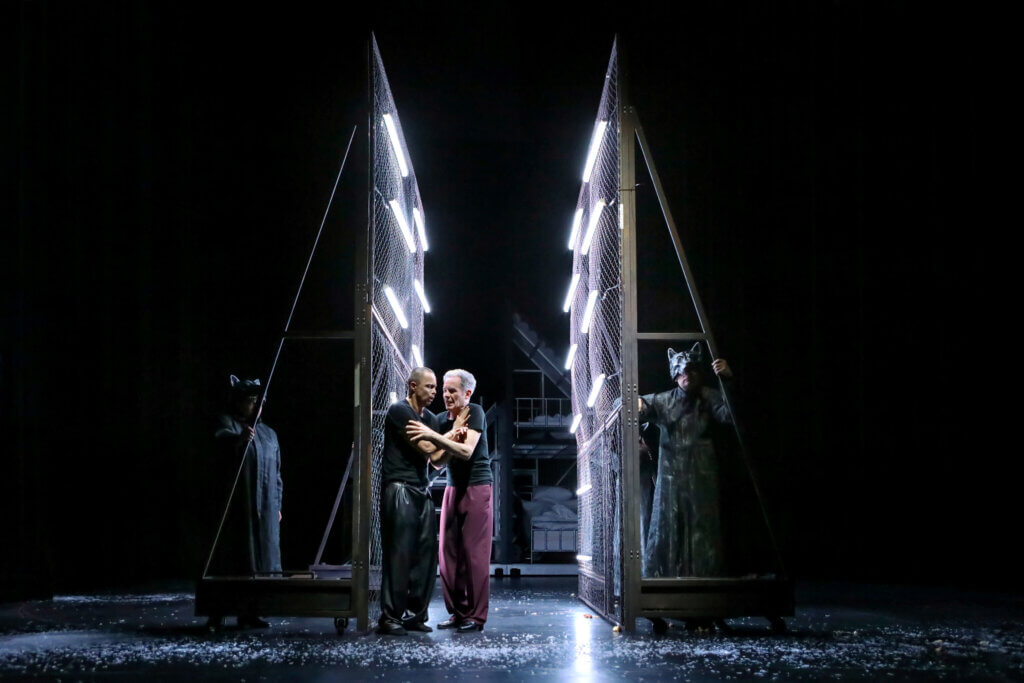 Peter und Ilya stehen aneinander gedrängt zwischen zwei beleuchteten Gitterwänden.