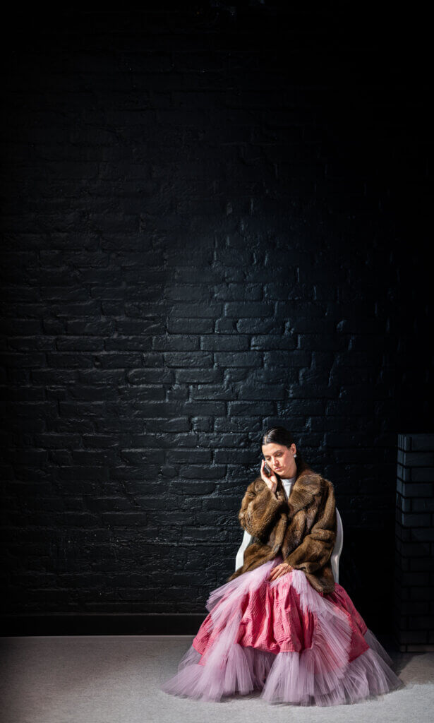 Eine Darstellerin vor einer dunklen Mauer, telefonierend