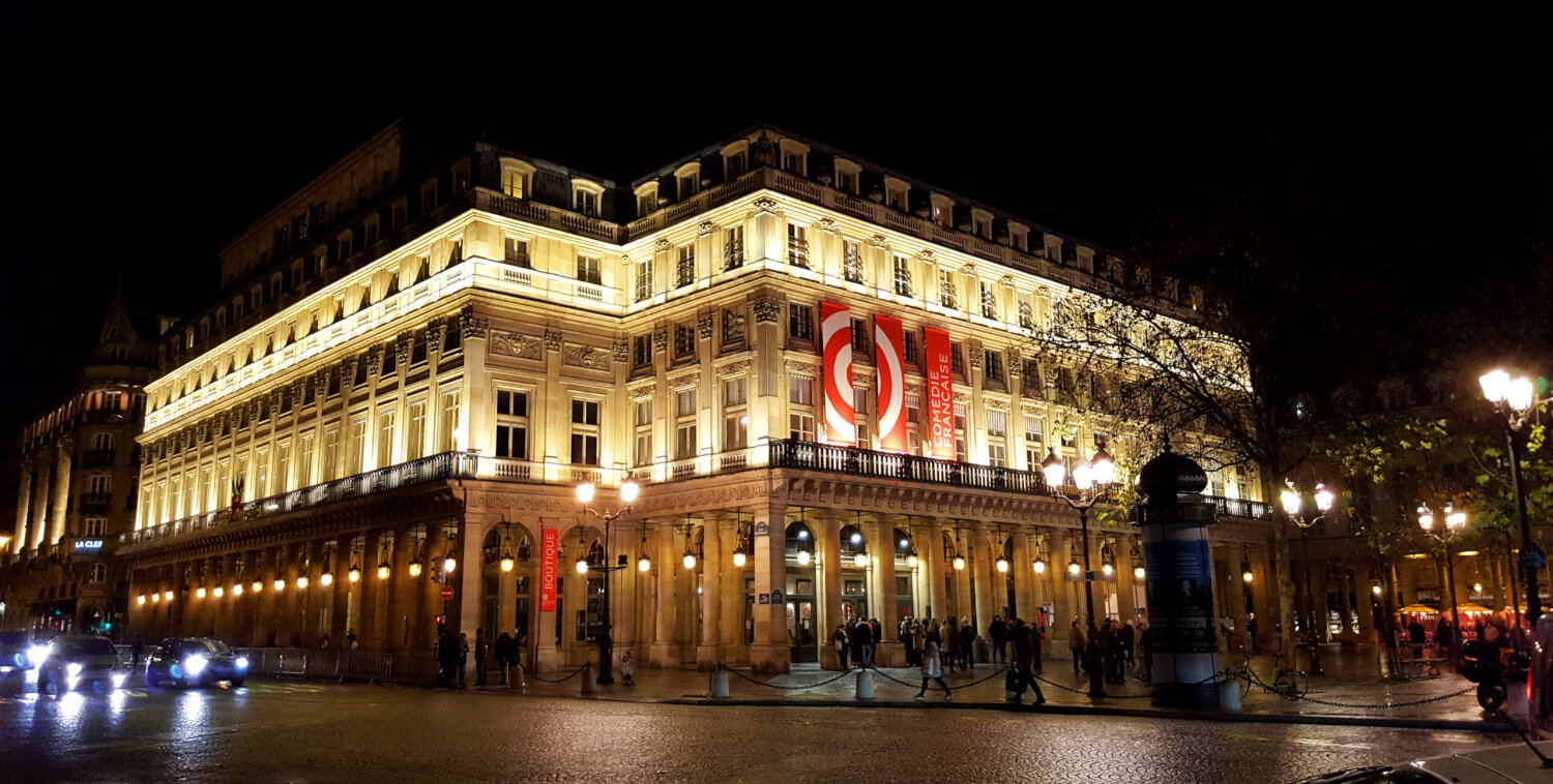 Die Comédie-Française in Paris. Das Gebäude bei Nacht, die Fassade in warmem Licht angestrahlt.