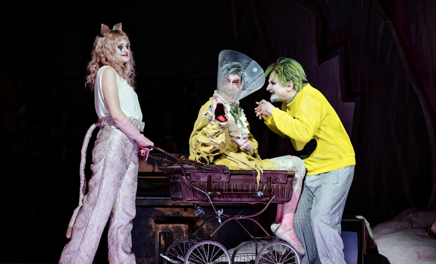 Alison Scherzer und Gyula Nagy schieben Timur in einem Kinderwagen. Timur trägt ein trichterförmige Halskrause aus Plastik.