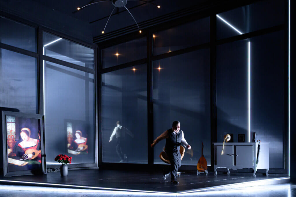 Pauls Zimmer ist auf der Bühne ein viereckiger Würfel, der in Neonlicht eingerahmt ist. Darin befindet sich ein historisch aussehendes Gemälde wie eine Kommode.