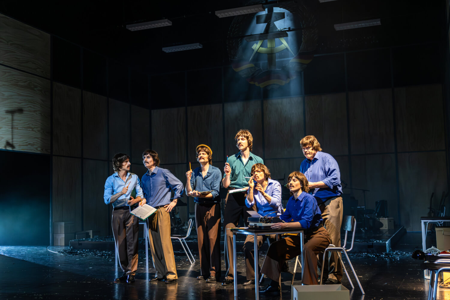 Aufführungsfoto von „Biermann – Drachentöter“ von Martin Heckmanns am Staatstheater Meiningen. Sieben Männer und Frauen, die alle wie Wolf Biermann aussehen, schauen nach vorne und halten einen Stift in der Hand.