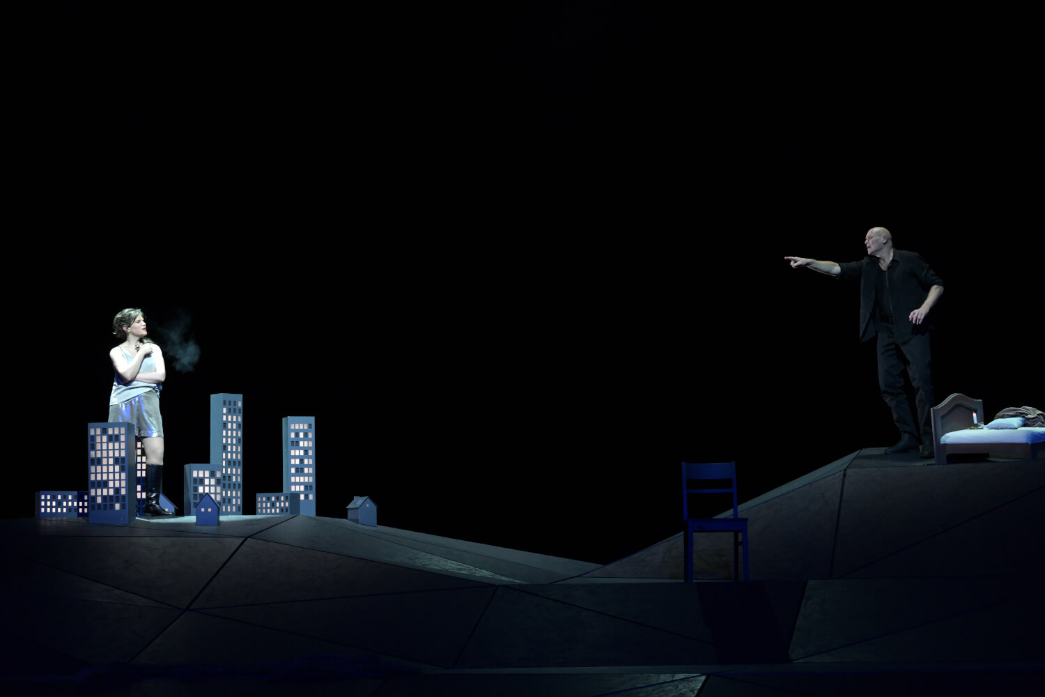 Elizabeth Reiter (Agnès) steht links inmitten von Miniatur-Hochhäusern. Rechts steht Bo Skovhus (The Protector) und zeigt aus dem Schatten anklagend auf sie.